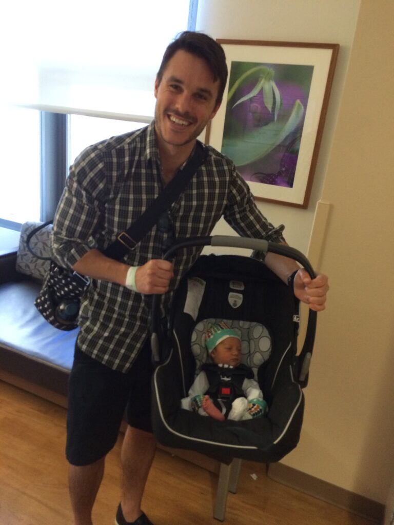 dad carrying baby in car seat. article about packing your hospital bag.